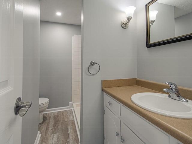 full bathroom featuring toilet, wood finished floors, baseboards, walk in shower, and vanity