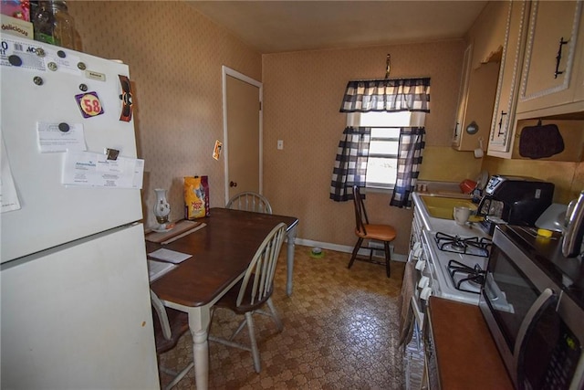 kitchen with stainless steel microwave, wallpapered walls, baseboards, freestanding refrigerator, and a sink