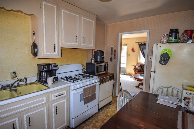 kitchen featuring wallpapered walls, light floors, white appliances, white cabinetry, and a sink