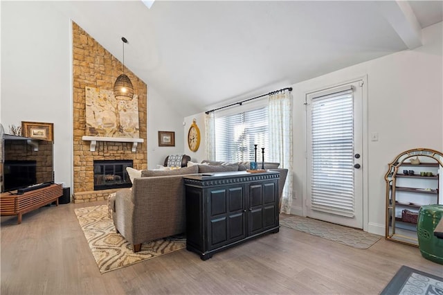 living room with baseboards, high vaulted ceiling, a stone fireplace, and wood finished floors