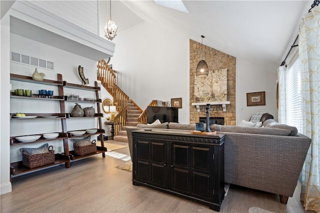 living room with visible vents, stairs, a fireplace, light wood-style floors, and a notable chandelier