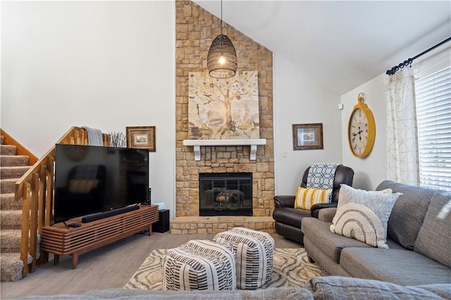 living area featuring a stone fireplace, high vaulted ceiling, stairs, and wood finished floors