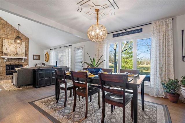 dining space with a stone fireplace, lofted ceiling with beams, an inviting chandelier, and wood finished floors