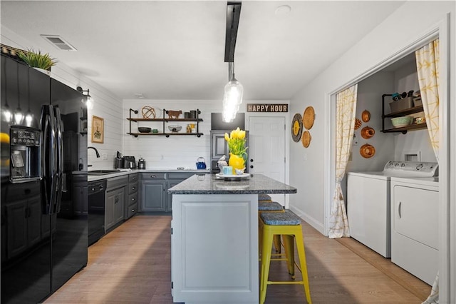 kitchen with light wood finished floors, washing machine and clothes dryer, open shelves, gray cabinetry, and black appliances