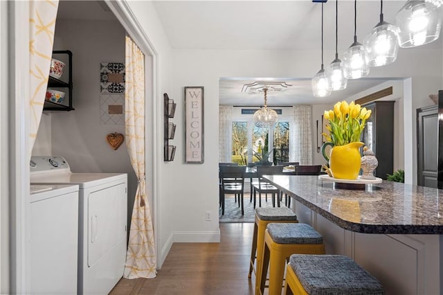 kitchen featuring a breakfast bar, decorative light fixtures, dark wood-style floors, separate washer and dryer, and baseboards