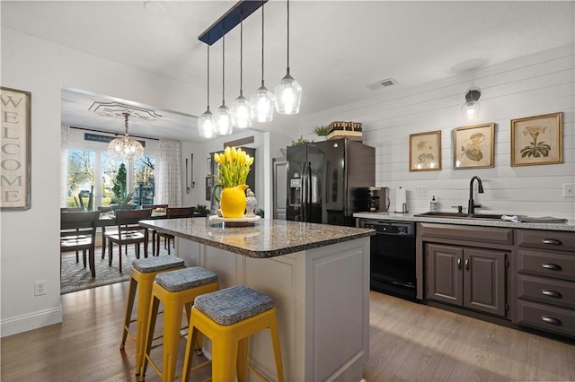 kitchen featuring visible vents, a kitchen island, a breakfast bar area, black appliances, and a sink