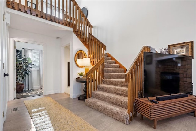 staircase featuring a high ceiling, wood finished floors, visible vents, and baseboards