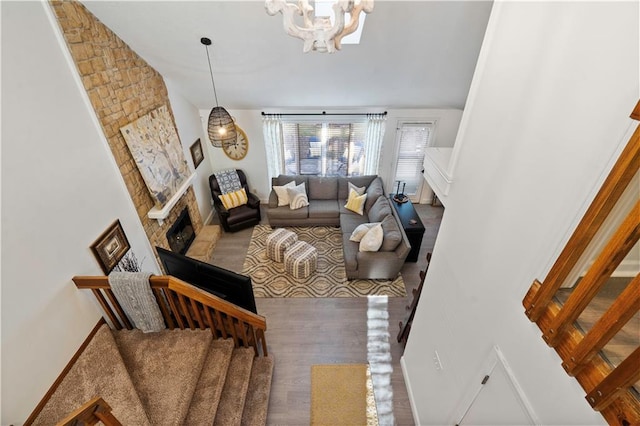 living room with a notable chandelier, wood finished floors, a stone fireplace, baseboards, and stairs