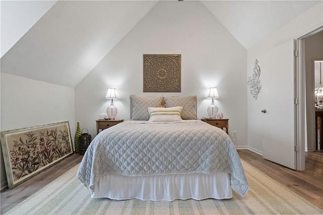 bedroom with vaulted ceiling, wood finished floors, and baseboards