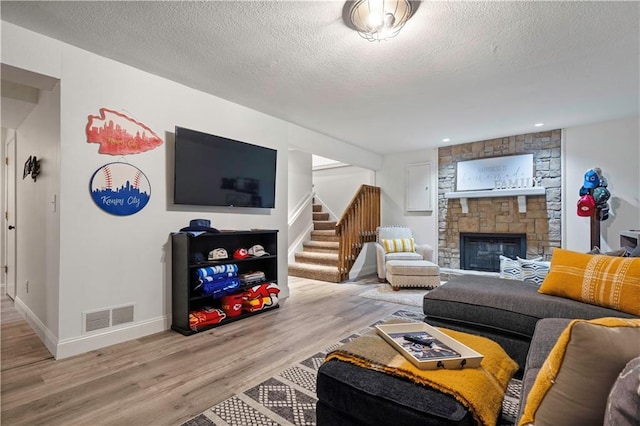 living area featuring visible vents, a textured ceiling, stairway, a stone fireplace, and light wood finished floors