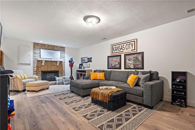 living room with visible vents, a fireplace, light wood-type flooring, and a textured ceiling