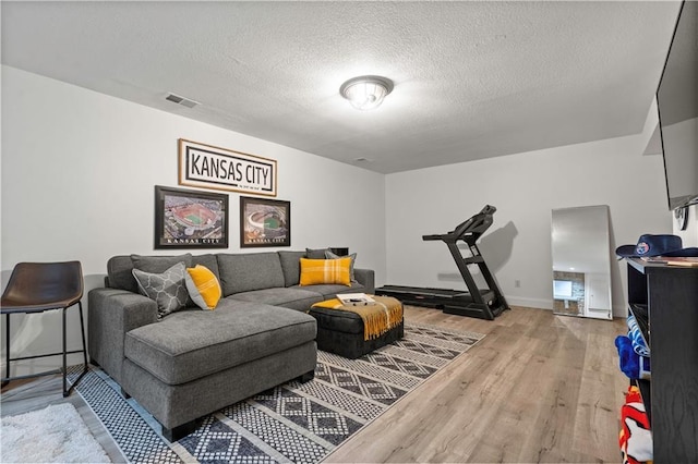 living room with baseboards, wood finished floors, visible vents, and a textured ceiling