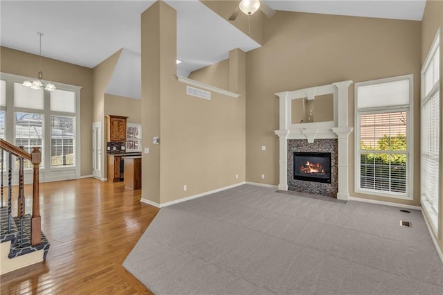 unfurnished living room featuring stairway, baseboards, high vaulted ceiling, a fireplace, and ceiling fan with notable chandelier