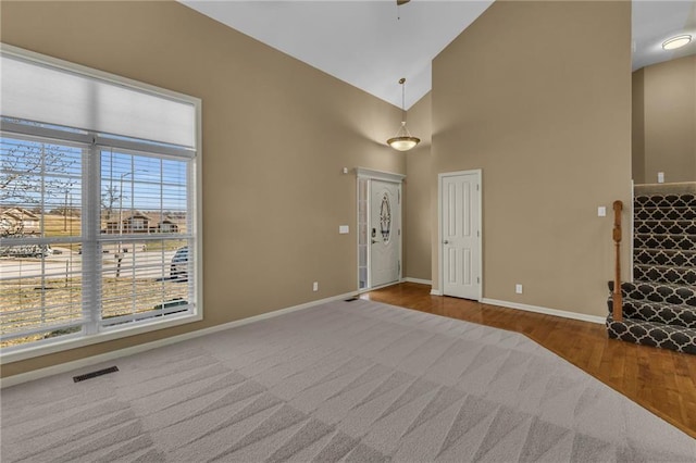 entrance foyer with visible vents, baseboards, high vaulted ceiling, and wood finished floors