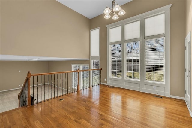 spare room featuring visible vents, baseboards, an inviting chandelier, and wood finished floors