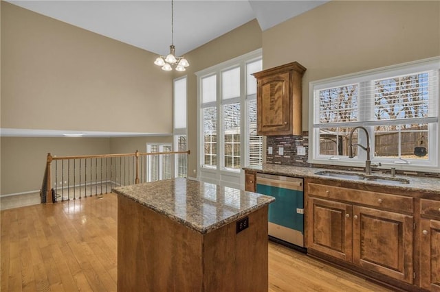 kitchen featuring a kitchen island, light wood-type flooring, dishwashing machine, dark stone countertops, and a sink