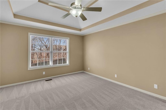 carpeted empty room with visible vents, crown molding, baseboards, a tray ceiling, and a ceiling fan