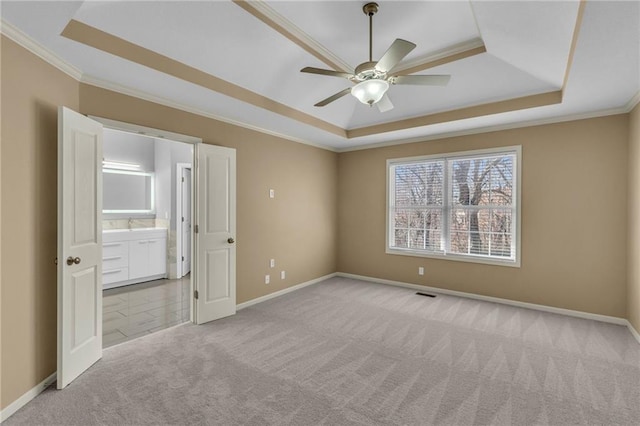 empty room with a tray ceiling, a ceiling fan, ornamental molding, and carpet flooring