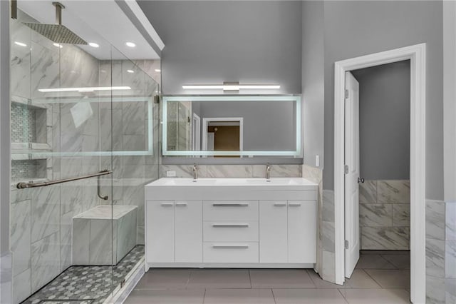 full bathroom featuring a marble finish shower, double vanity, tile walls, and a sink