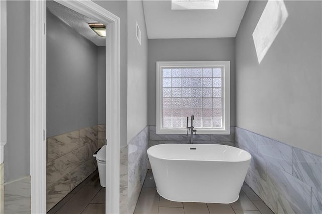 bathroom featuring a freestanding tub, visible vents, toilet, tile walls, and wainscoting