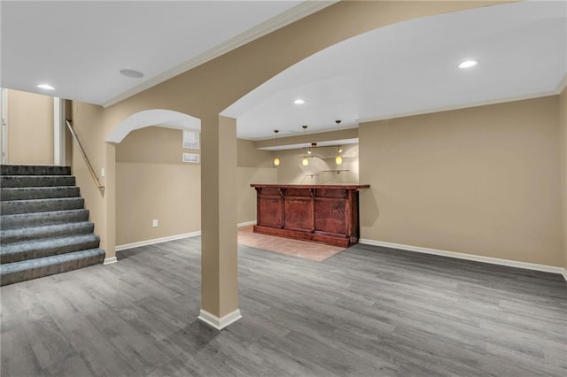 unfurnished living room featuring arched walkways, crown molding, baseboards, and wood finished floors