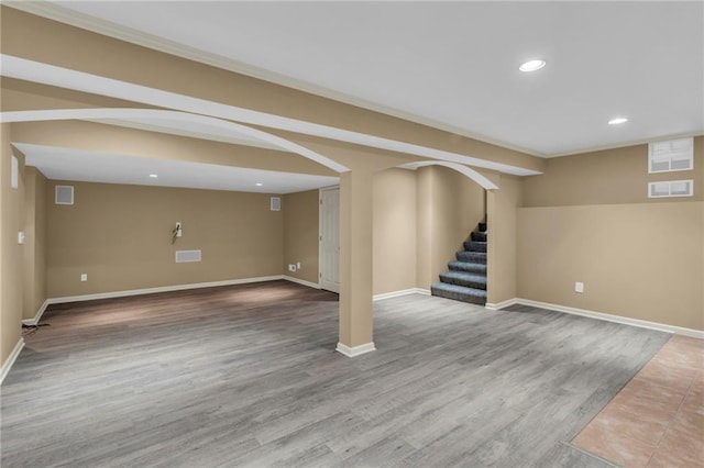 finished below grade area featuring visible vents, stairway, recessed lighting, wood finished floors, and arched walkways