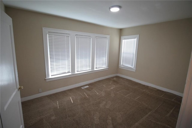 empty room featuring dark colored carpet, visible vents, and baseboards