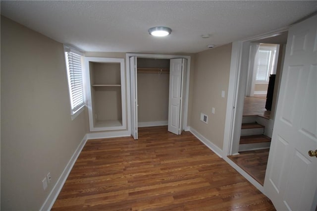 unfurnished bedroom with visible vents, a textured ceiling, baseboards, and wood finished floors