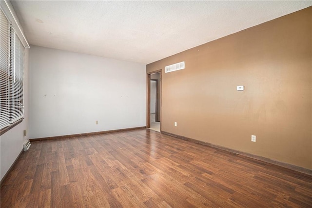 empty room featuring baseboards, wood finished floors, visible vents, and a textured ceiling