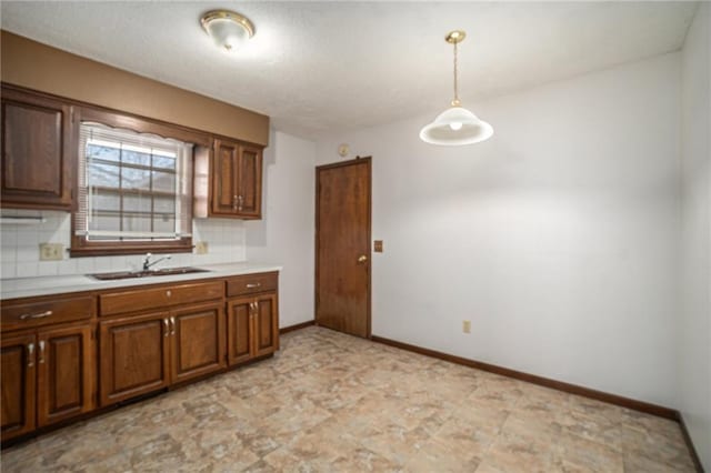 kitchen with baseboards, a sink, light countertops, pendant lighting, and tasteful backsplash