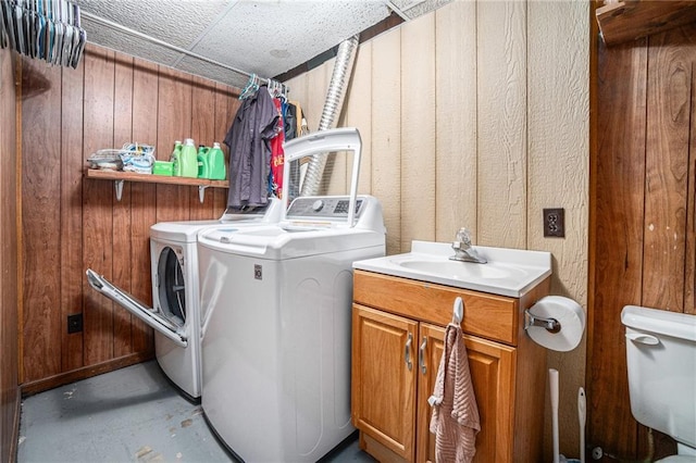 laundry room featuring laundry area, wooden walls, washing machine and dryer, and a sink