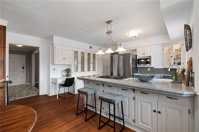 kitchen with a peninsula, a sink, dark wood-type flooring, glass insert cabinets, and appliances with stainless steel finishes