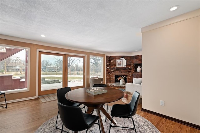 dining room with light wood finished floors, a brick fireplace, baseboards, recessed lighting, and a textured ceiling