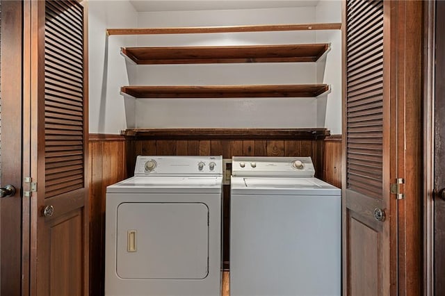 clothes washing area featuring separate washer and dryer, wood walls, wainscoting, and laundry area