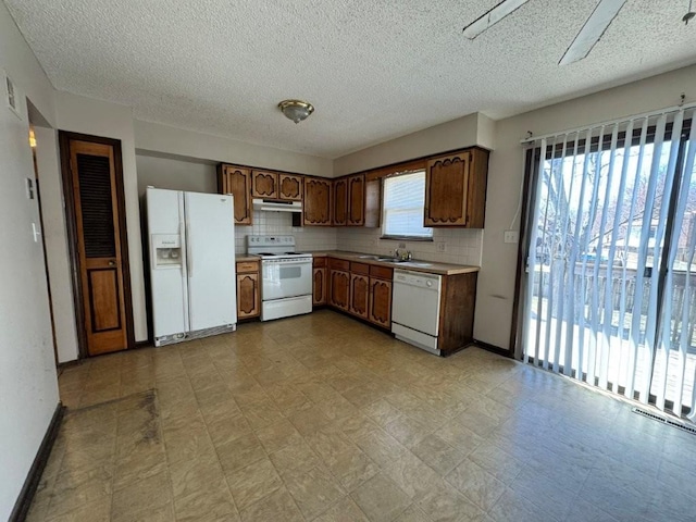 kitchen with under cabinet range hood, tasteful backsplash, white appliances, light countertops, and light floors