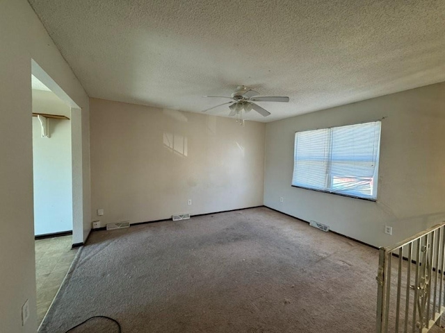 carpeted spare room featuring visible vents, a textured ceiling, and ceiling fan