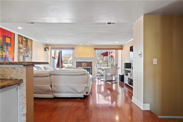 living room featuring visible vents, crown molding, wood finished floors, a glass covered fireplace, and a textured ceiling