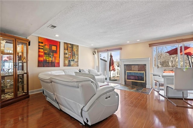 living room with wood finished floors, baseboards, visible vents, a textured ceiling, and a tiled fireplace