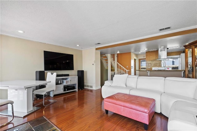 living area featuring wood finished floors, visible vents, stairs, a textured ceiling, and crown molding