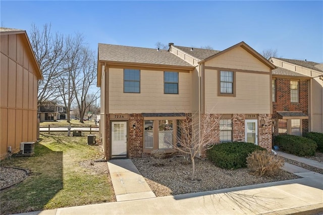 view of property featuring central AC unit, brick siding, and a shingled roof