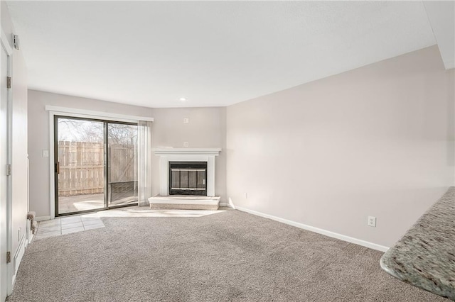 unfurnished living room featuring a glass covered fireplace, baseboards, and carpet