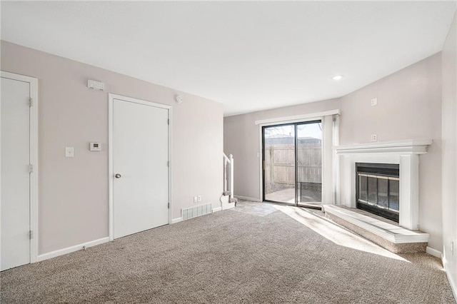 unfurnished living room with visible vents, carpet flooring, baseboards, and a glass covered fireplace