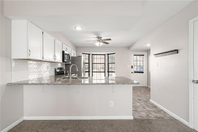 kitchen featuring tasteful backsplash, a peninsula, stainless steel appliances, a ceiling fan, and a sink