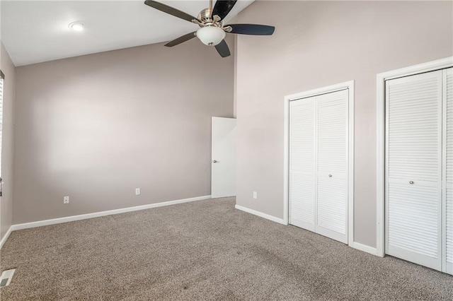 unfurnished bedroom featuring two closets, baseboards, ceiling fan, carpet, and high vaulted ceiling