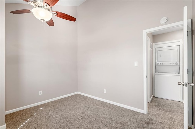 empty room featuring stacked washer / dryer, light colored carpet, a ceiling fan, and baseboards