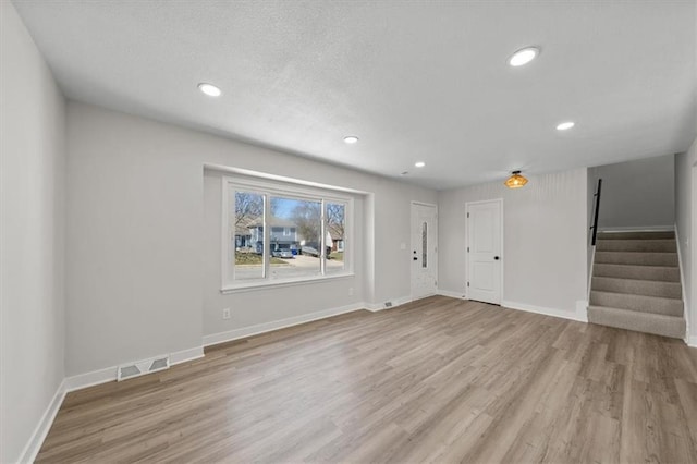 unfurnished living room featuring visible vents, light wood-style flooring, recessed lighting, stairway, and baseboards