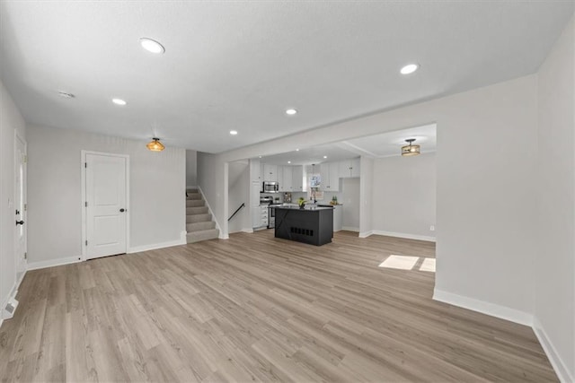 unfurnished living room with stairs, baseboards, and light wood-type flooring