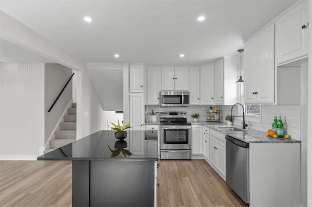 kitchen featuring dark stone countertops, light wood finished floors, a sink, stainless steel appliances, and white cabinets