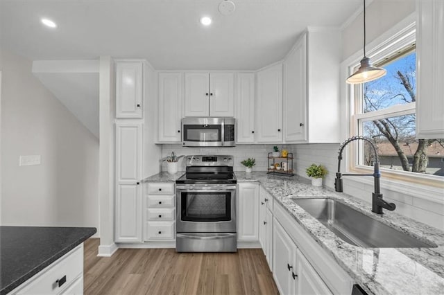 kitchen featuring a sink, tasteful backsplash, white cabinetry, appliances with stainless steel finishes, and light wood finished floors