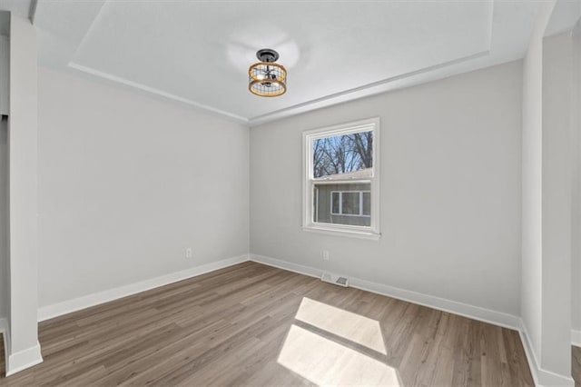 empty room with wood finished floors, visible vents, and baseboards